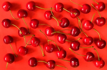 Foto op Plexiglas sweet cherries layed out as pattern on red background,flat lay © Kirsten Hinte