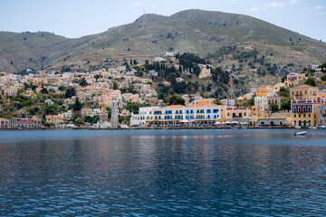 Fototapeta na wymiar A View From the Water of the Harbor of Symi with Its Clock Tower, Colorful Houses, Small Hotels, and Restaurants Filled with People