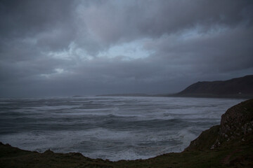 Rhossili Bay at dusk during a winter's storm with dramatic skies, wind and rain. Rhossili Downs are covered with bracken and waves are pounding the beach at high tide.