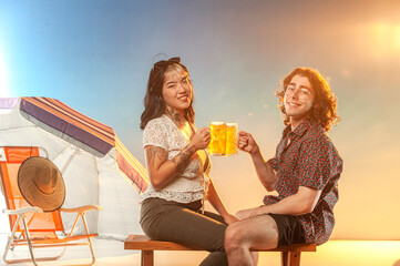 Interracial couple toasting draft beer against the sunset.