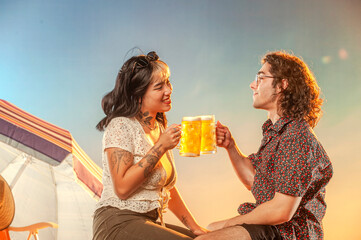 Interracial couple toasting draft beer against the sunset.