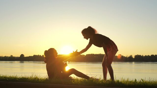 Silhouette of girl giving helping hand to her friend during training. Woman supports and helps another sportsman with trauma or health problems after running. Mutual assistance and teamwork in sport.