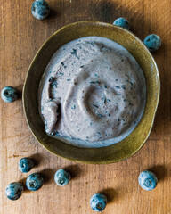 Blueberry gelato inside a handmade ceramic bowl on a worn wooden board, with some blueberries around