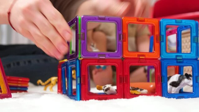 The nanny spends time in a modern cozy house with a little boy. Loving caring mother plays with her preschool son, builds a tower of magnetic blocks. Child development, play time concept
