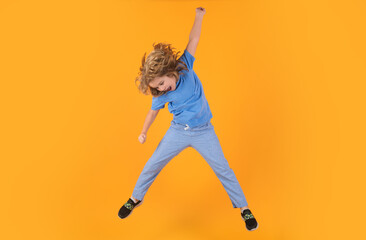 Fototapeta na wymiar Funny boy jumping. Energetic kid boy jumping and raising hands up on isolated studio background. Full length body size photo of jumping high child boy, hurrying up running fast on yellow background.