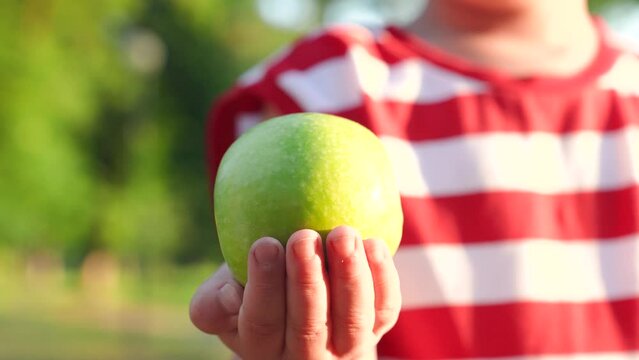 Green apple on childs hand in garden, closeup. Boy holds green fresh apple in his hand. Vitamins for kid, tasty fruits, healthy food. Family, food for healthy child, hand with delicious juicy apple