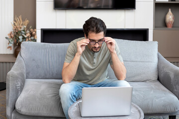 Handsome man sitting on the couch and working on laptop at home. Online education and distant work concept