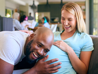 Couple With Man Listening To Pregnant Woman's Stomach On Sofa At Home With Multi-Generation Family  - Powered by Adobe