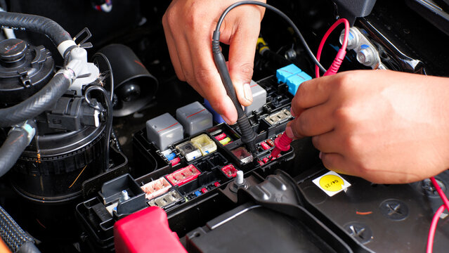 car mechanic checking the fuse connection using a multimeter and a test pen in the car fusebox
