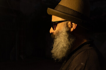 Retrato de costado hombre a la moda usando barba sombrero y gafas para el sol