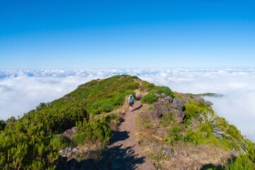 Fototapeta na wymiar Una senderista sobre una montaña se dirige hacia un mar de nubes al horizonte en la isla de Madeira, Portugal.