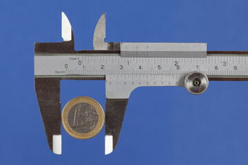 Euro coin in a caliper. How can you measure the value of money..