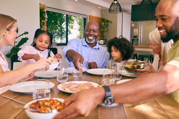 Multi-Generation Family Sitting Around Table Serving Food For Meal At Home 