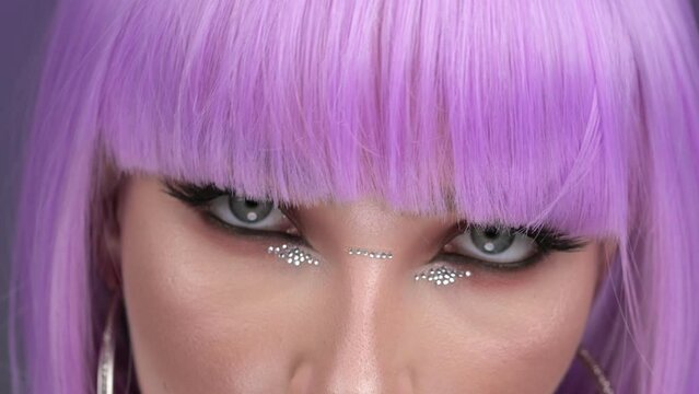 A luxury model in a purple wig poses in the studio. Close-up, eyes. Purple background. 4K, 30fps
