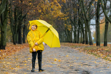 Full-length portrait of child on autumn park background. Child in raincoat with yellow umbrella