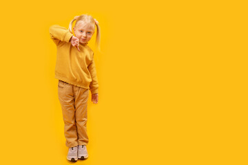 Full length portrait of girl shows finger down. Child of 4-5 years old in yellow suit on bright yellow background . Copy space, mock up