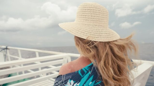 Anonymous blonde woman with long hair and straw hat sitting on upper deck of ferry ship motorboat enjoying freedom and wind in open sea. Female person on ocean cruise voyage on summer vacation. Free.