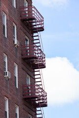 red art-deco fire escapes with curved railings on a red brick building against the sky with a fluffy white cloud, making it appear the fire escapes lead to the sky, vertical portrait orientation