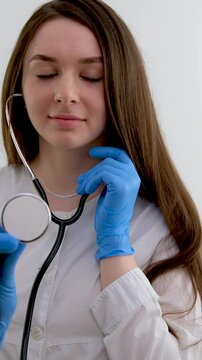 Blur portrait of young alluring nurse with long hair in white medical uniform with focus on stethoscope on neck standing on yellow background copyspace, horizontal picture. High quality photo