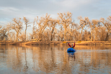 senior male is paddling an inflatable packraft on a calm lake with heron rookery in early spring in northern Colorado