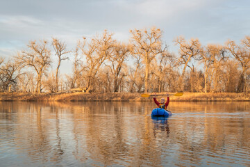 Fototapeta premium senior male is paddling an inflatable packraft on a calm lake with heron rookery in early spring in northern Colorado