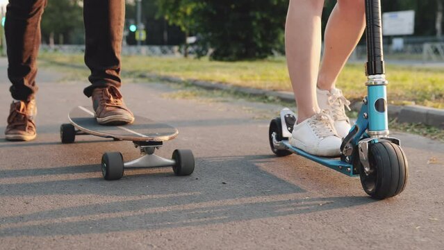 Teens ride skateboard or longboard and scooter together. Close-up of foot, shoes, sneakers. Skating on asphalt track in the city. Skateboarding at summer. Concept of youth, active lifestyle.