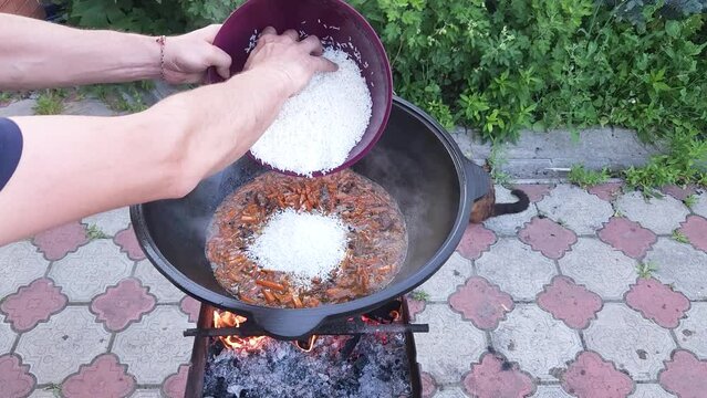 Cooking Uzbek pilaf. Adding Laser rice to boiling zirvak in a cast-iron cauldron on the grill