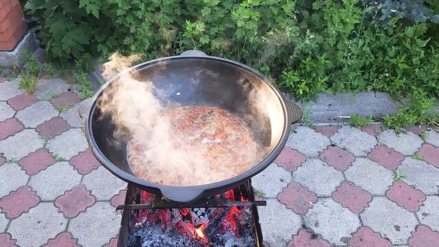 Cooking Uzbek pilaf. Boiling zirvak in a cast-iron cauldron on the grill