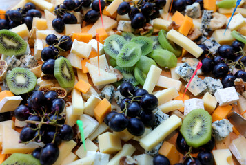 Assorted cheeses on a plate.Parmesan cheese, blue cheese and brie on a plate with grapes, kiwi and figs. Top view and selective focus.