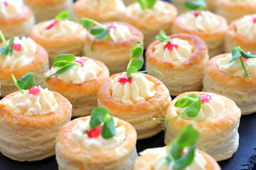 Appetizer puff pastry stuffed with soft cream cheese decorated with fresh micro plants. Selective focus.