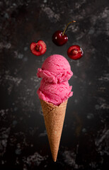 Red ice cream in a waffle cone with cherries on a dark background