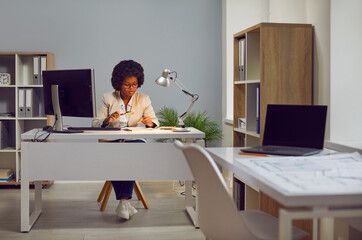 Young african american woman auditor checking financial documents with magnifying glass over office...