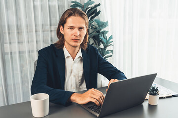 Businessman in black suit working on laptop at his workspace desk. Smart executive researching financial data and planning marketing strategy on corporate laptop at modern workplace. Entity