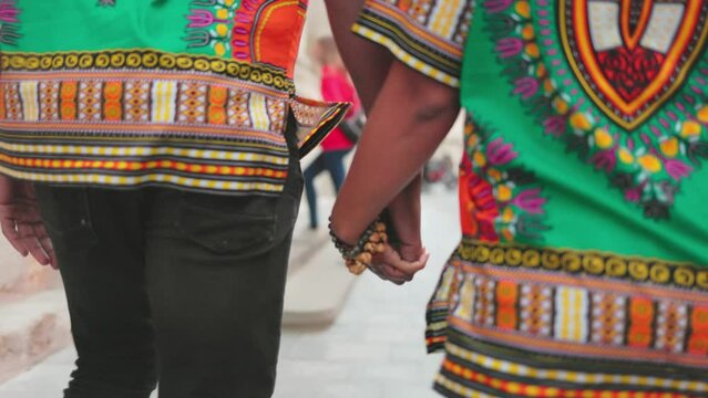 Detailed shoot of human hands holding each other. Close up image of man's hand in bracelet holding woman's hand. Couple in bright outfit hold hands and move. Portrait of intertwined human fingers.