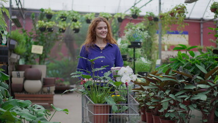 Happy Woman in walking through Horticulture Store aisle. Female Shopper with shopping Cart searching for Plant Purchases