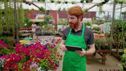 Green-Aproned Man Leveraging Tablet for Inventory in Flower Shop. Young Male Employee Engaging with Modern Tech
