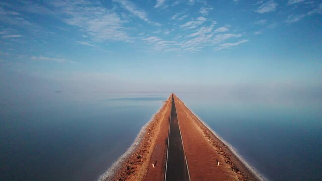 4K aerial view of beautiful road and salt water lake on both sides, connecting Khavda to Dholavira in Kutch, Gujarat, India. Road to heaven. Road trip. Clouds in sky with infinite road.