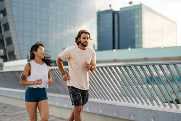 Cheerful young multi-ethnic urban couple running alongside the beach wearing casual summer sport clothing. Jogging in the city