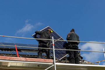 Craftsmen install a new photovoltaic system on a roof under a blue sky
