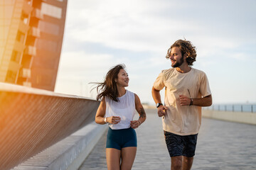 Cheerful young multi-ethnic urban couple running alongside the beach wearing casual summer sport clothing. Jogging in the city