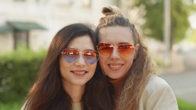 Lesbian girls hug, smile and show positive face emotions. Portrait of two young smiling hipster women friends wearing sunglasses of heart shape. LGBTQI, Pride Event, LGBT Pride Month, Gay Pride Symbol