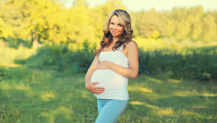Fototapeta na wymiar Portrait of happy young pregnant woman walking in summer park