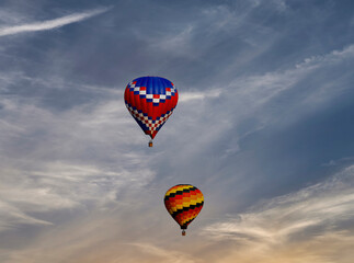 A View of Two Multi Colored Hot Air Balloons Floating in a Beautiful Blue Sky With Thin Clouds © Greg Kelton