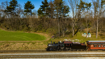 A Drone View of a Restored Steam Passenger Train Traveling Thru Farmlands Pulling Up to a Small Station on an Autumn Day