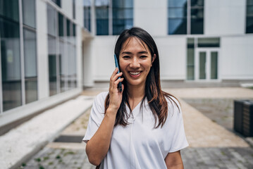 Young busy successful beautiful Japanese business woman, Japanese professional businesswoman holding cellphone using smartphone standing or walking on big city urban street outside