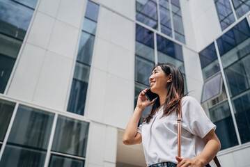 Young busy successful beautiful Japanese business woman, Japanese professional businesswoman holding cellphone using smartphone standing or walking on big city urban street outside