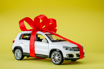 White model car with bow on a yellow background. Car as gift, surprise