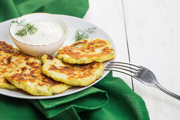 Vegetable zucchini pancakes in plate and cream sauce. Dish on green napkin.