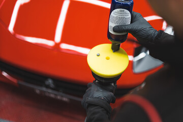 Polishing product distributed onto orbital polisher. Closeup shot with blurred red sports car in the background. High quality photo