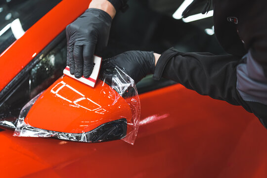 The process of installing PPF on the side mirror of a red sports car. Protective film for paint protecting scratches and gravel. High quality photo